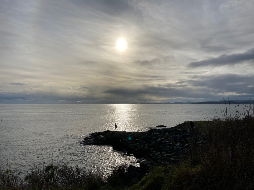 Person standing on a point at the shore. They appear as a silhouette. A beam of light appears behind them on the water.