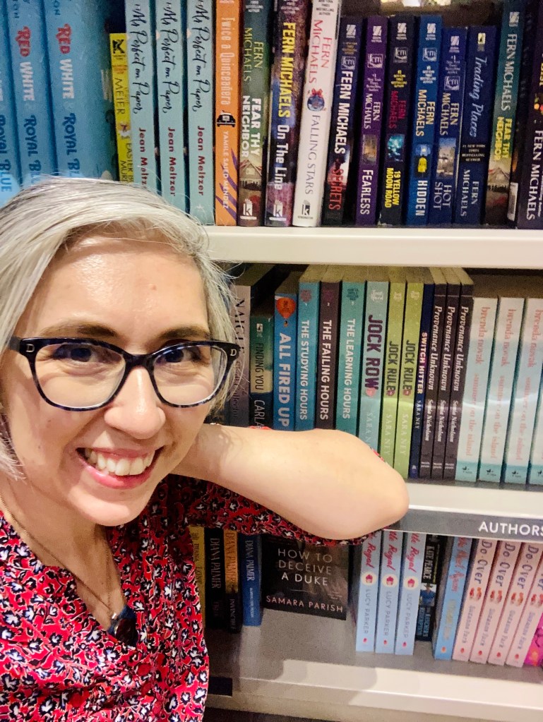 Smiling woman beside full bookstore shelf.