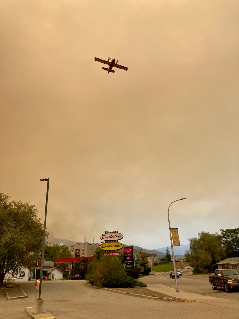 Water bomber aircraft flying through smoky skies over a Tim Hortons.