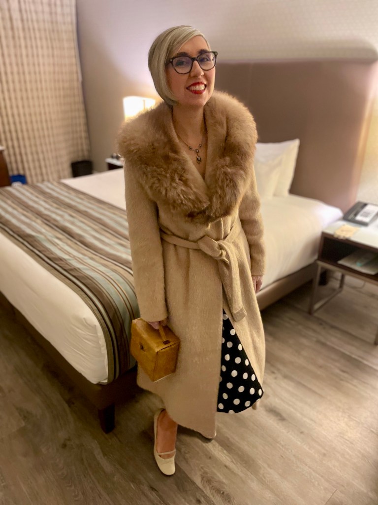 Sonia Nicholson dressed in 1950s-inspired evening wear including long coat, polka dot dress, and purse.