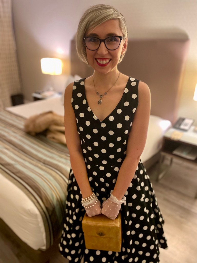 Sonia Nicholson dressed in 1950’s-inspired evening wear, including polka dot dress, and purse.
